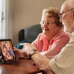 Two seniors citizens sitting at a table talking to two children on a tablet