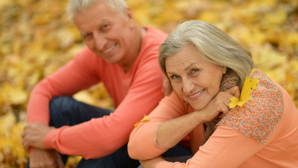 happy older adults sitting in the autumn leaves