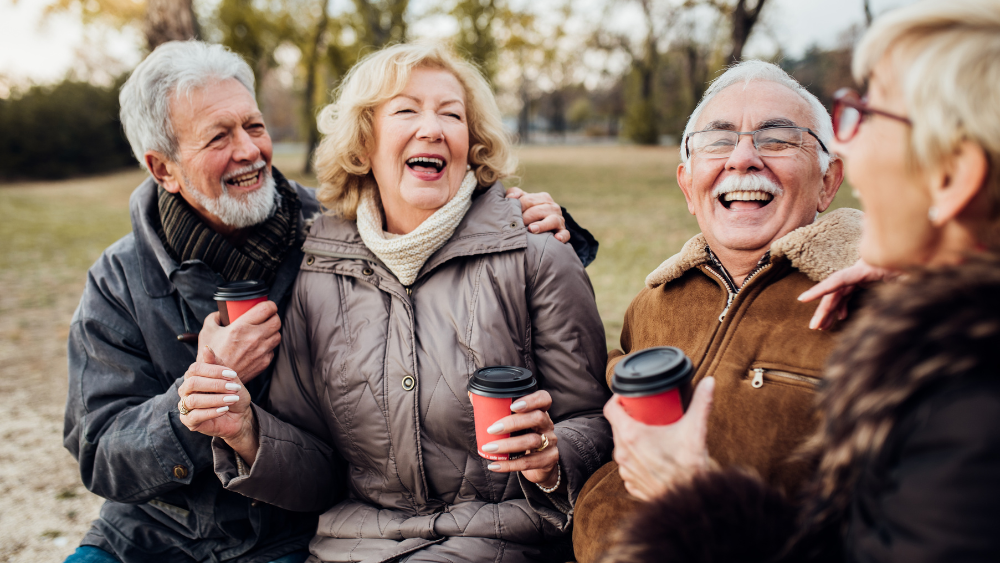 four old people sitting outside laughing and drinking coffee in the fall